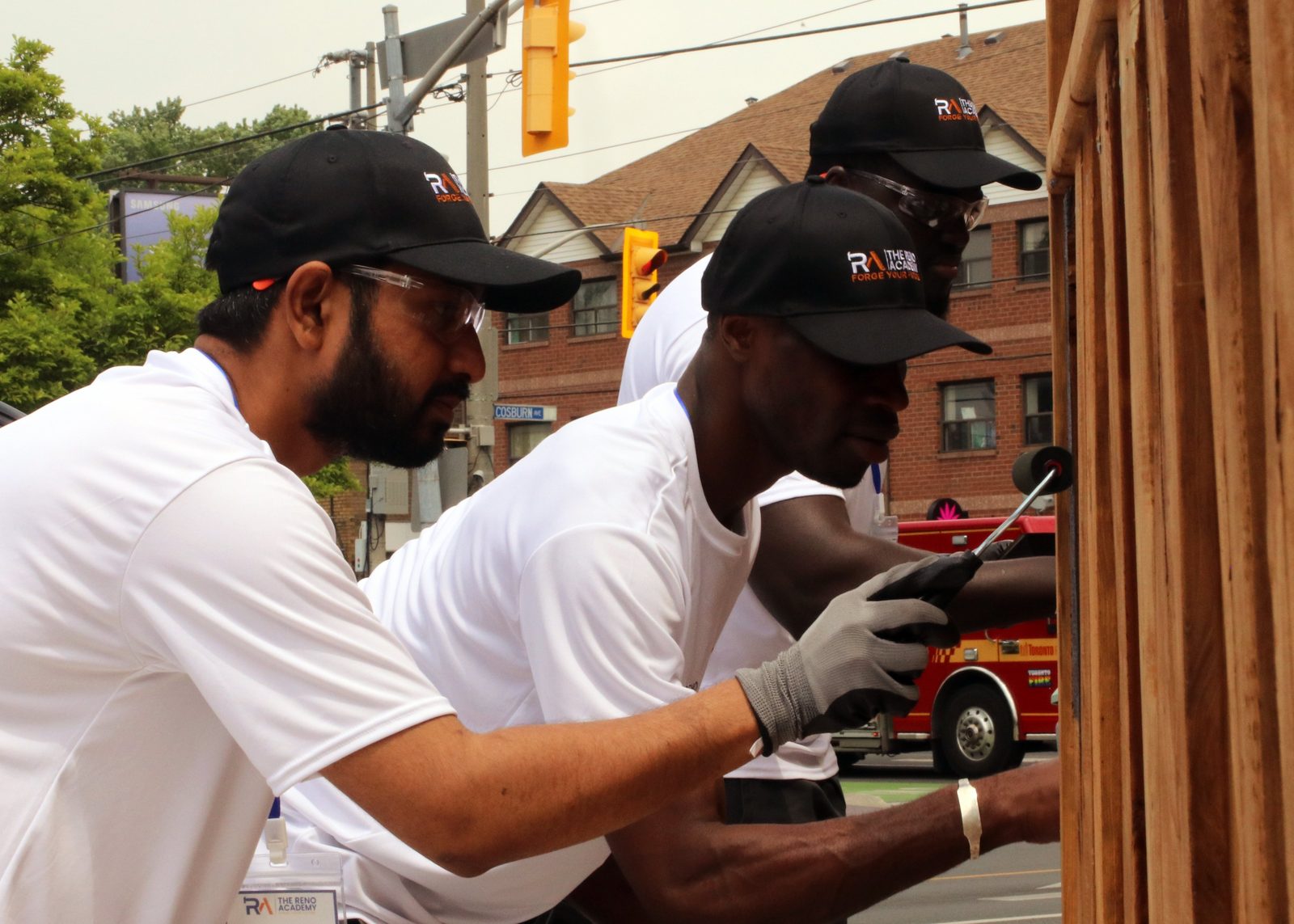 Three Site Squad Bootcamp LE students hammering fence boards on a Toronto street during outdoor trades training